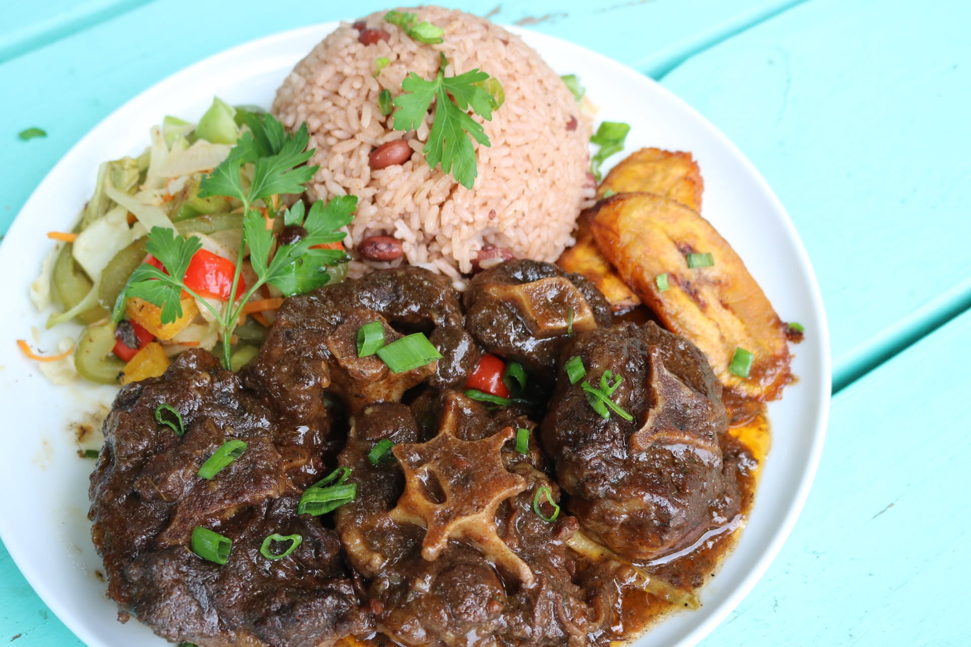 Oxtail in gravy with rice and peas, cabbage and fried plantain